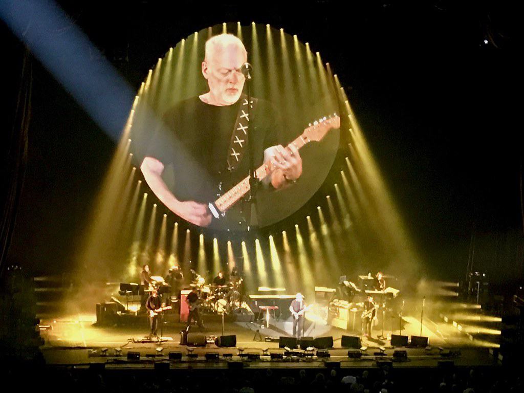 a band on stage with a large screen with a picture of a man playing guitar