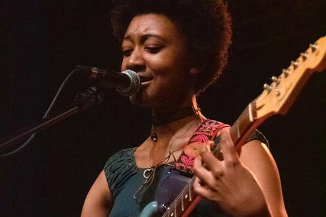 melanie faye singing into a microphone and playing guitar