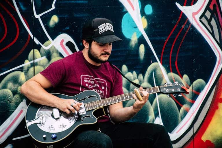 A guitarist plays a resonator guitar against a colorful graffiti background, creating an urban artistic vibe.