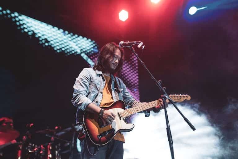 An Asian musician with long hair plays electric guitar during a live concert in Sibolga, Indonesia.