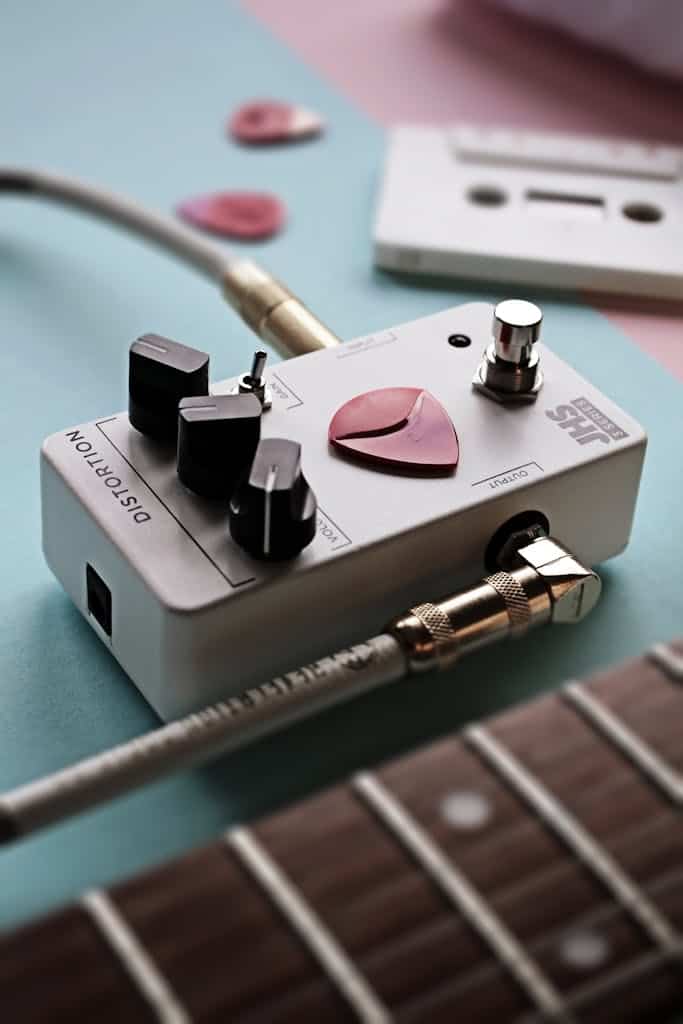 Close-up of a distortion pedal with guitar picks and a cassette on a pastel background.
