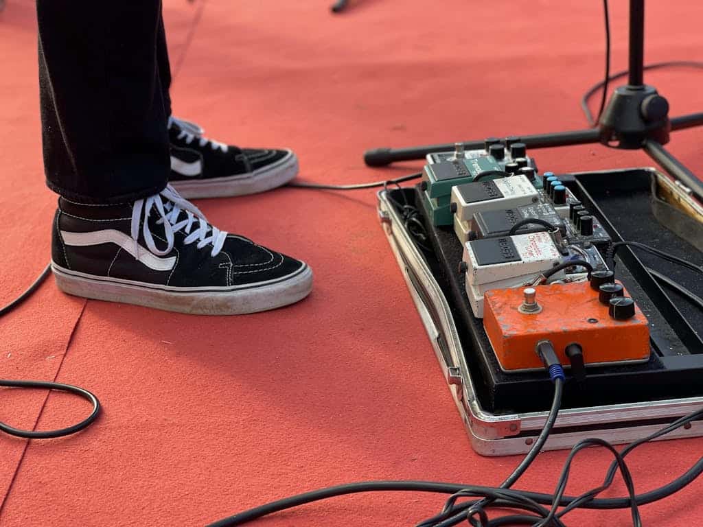 Close-up of a musician's foot operating a pedalboard on stage with vibrant lighting.