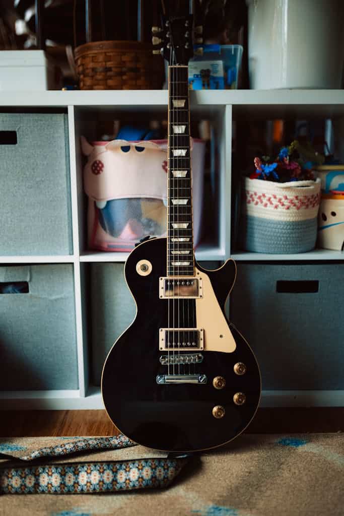 a black electric guitar leaning against a shelf