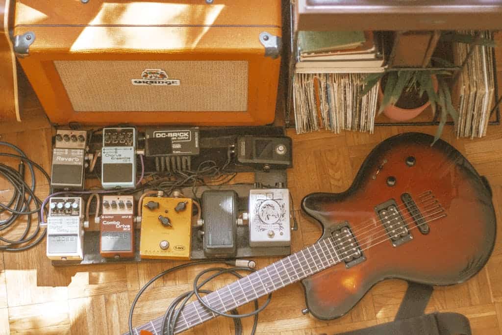 Vintage electric guitar and amplifier setup with various effects pedals on a wooden floor.